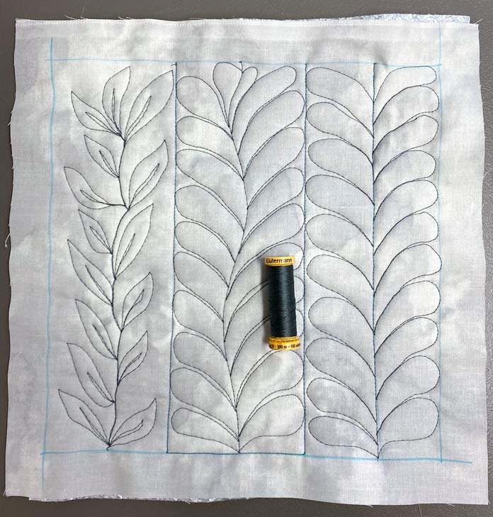 Feather and leaf free motion quilting Designs on grey fabric with a spool of black thread lying on top; Gütermann Thread