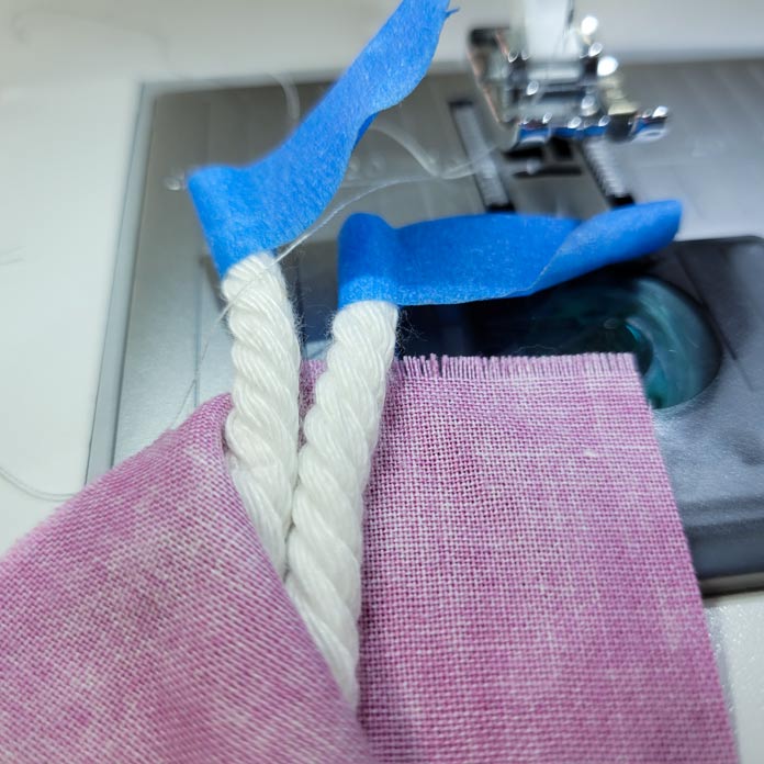 Two lengths of white cord inside the fold of pink fabric with blue painter’s tape securing the ends of the cord; Husqvarna Viking Opal 670