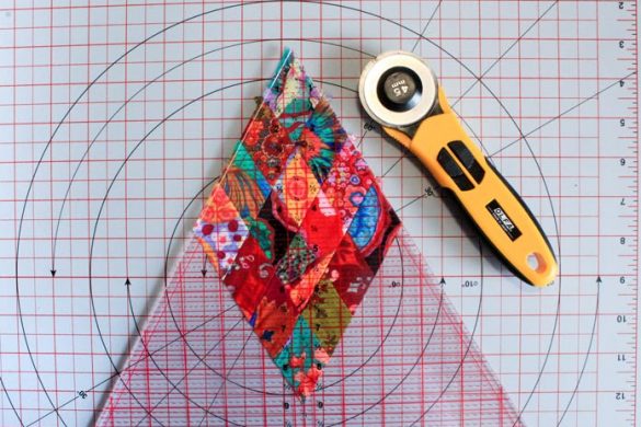 Trimming off excess fabric on the edge of the 16-patch diamond using the Sew Easy Triangle Ruler 60° a triangle ruler and a cutting mat; Komfort Kut 360° Rotating Cutting Mat - 18" x 18", OLFA Quick Change Rotary Cutter