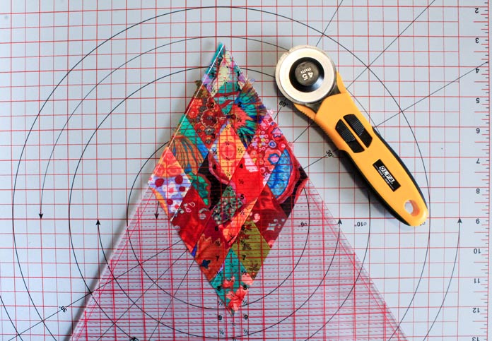 Trimming off excess fabric on the edge of the 16-patch diamond using the Sew Easy Triangle Ruler 60° a triangle ruler and a cutting mat; Komfort Kut 360° Rotating Cutting Mat - 18" x 18", OLFA Quick Change Rotary Cutter