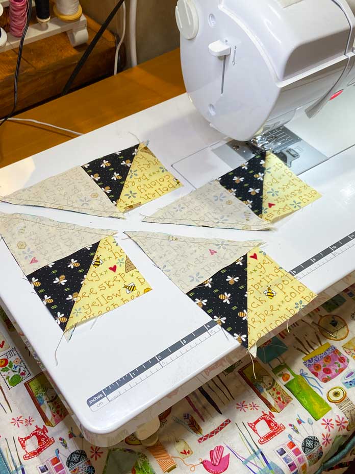Four pieced black and yellow units for the flying geese block shown on the extension table of the Brother NQ900 sewing machine. 
