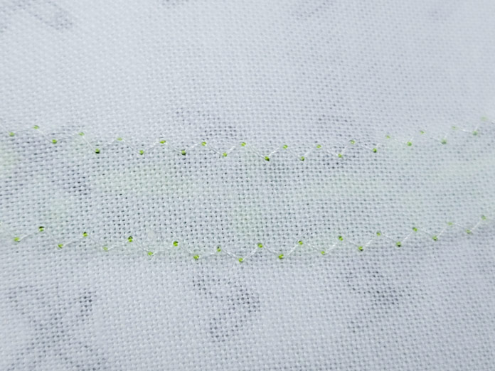 A line of stitches in white thread on white fabric