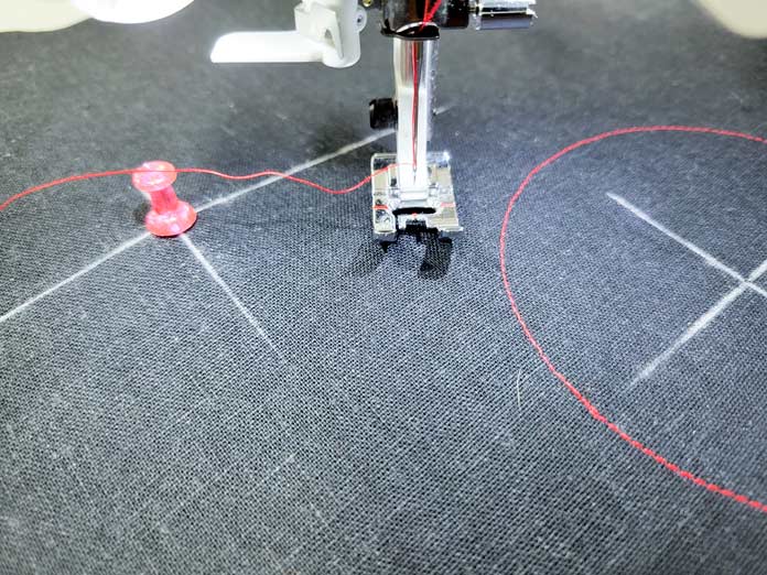 A pink push pin in the middle of white chalk lines on black fabric; Husqvarna Viking Tribute 150C