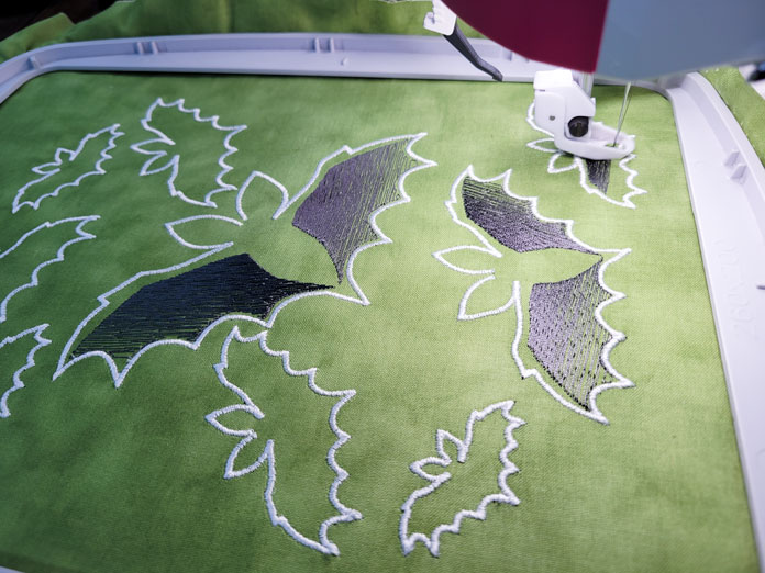 Gray and white stitching of bats on green fabric in a machine embroidery hoop; Husqvarna Viking Designer EPIC 2