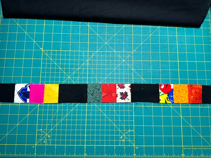 Black rectangles and 2” x 2” squares are sewn into a long row. 