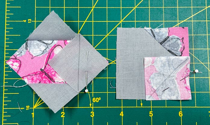 Two pieced squares made up of pink and gray fabrics sit on top of a green cutting mat.