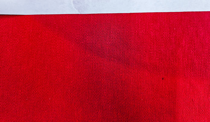 A white strip on the edge of a red fabric; Learn how to use HeatnBond SOFTSTRETCH fusible web on knits, denim, fleece, and more