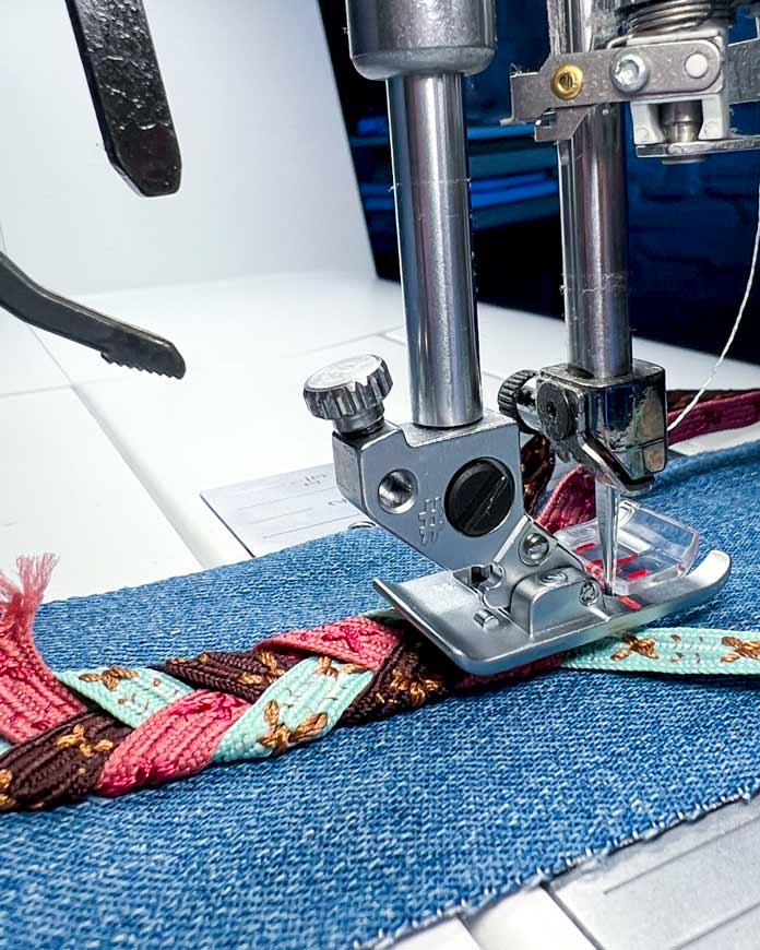 Side view of the 2A Fancy Stitch Foot on the PFAFF creative icon 2, showing how the ribbon is folding under the foot to create the Triple Ribbon Stitch #8.3.8 braided pattern on denim.