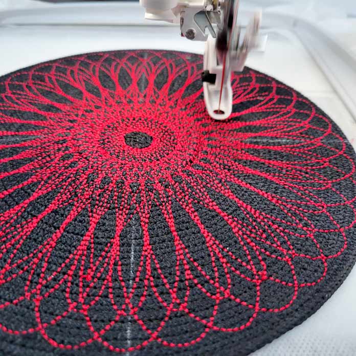 An embroidered spiro design stitched in red thread on black cording; Husqvarna Viking Designer Ruby 90 sewing and embroidery machine, Husqvarna Viking Extension Table with Adjustable Guide, Inspira Top Stitch Needles, Husqvarna Viking Multi-Function Foot Control, Inspira Fusible Fleece Stabilizer
