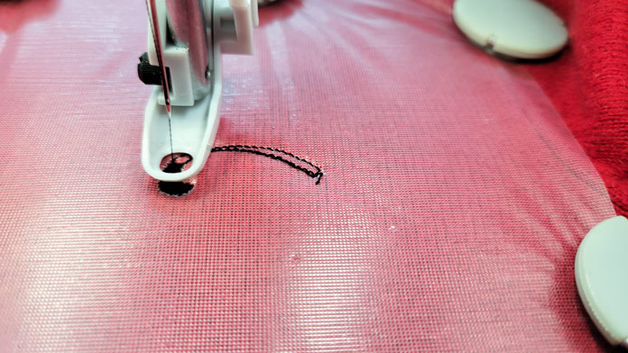 Machine stitching the embroidery with an embroidery foot and black thread on red fleece with a film topper stabilizer in a metal hoop; Inspira Water Works Soluble Film, Small Metal Hoop (100m x 100m), Inspira Magnets for Metal Hoop