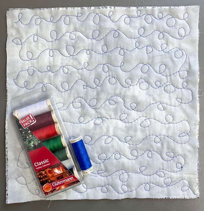 Free motion quilted e’s and o’s, with a package of Gütermann Classic Holiday Collection thread and a spool of blue thread.