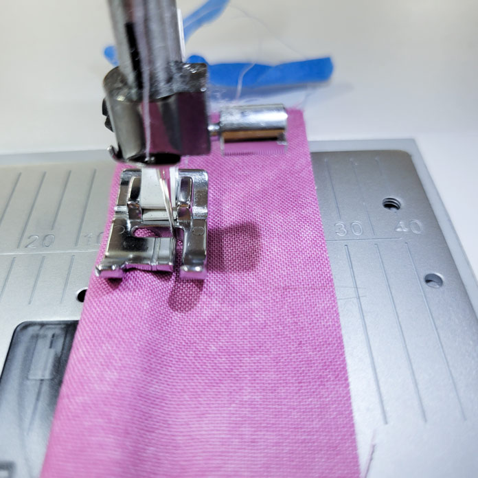 Pink fabric with two lengths of cord inside under a metal presser foot on a sewing machine; Husqvarna Viking Opal 670, Husqvarna Viking Single Welt Cord Foot