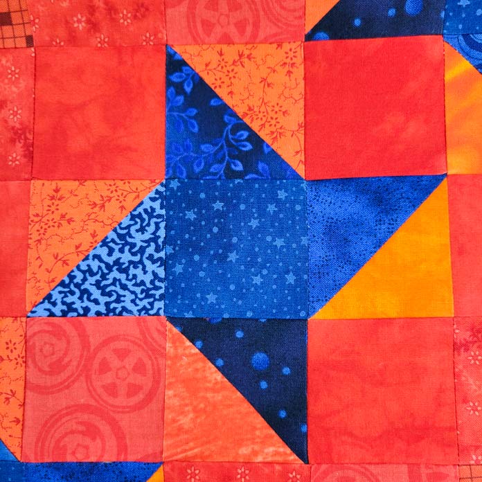 A pieced block of a blue star on orange fabric