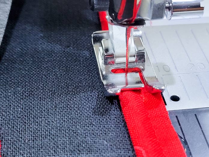 A strip of red fabric on a black fabric under the presser foot of a sewing machine; Husqvarna Viking Tribute 150C