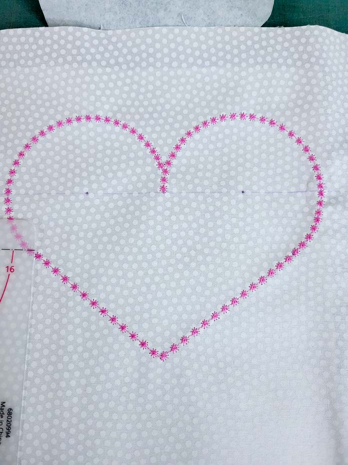A heart stitched in pink thread on white fabric