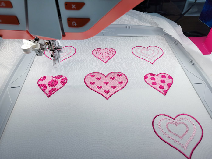 Seven pink hearts on white fabric in a machine embroidery hoop; Husqvarna Viking DESIGNER EPIC 2