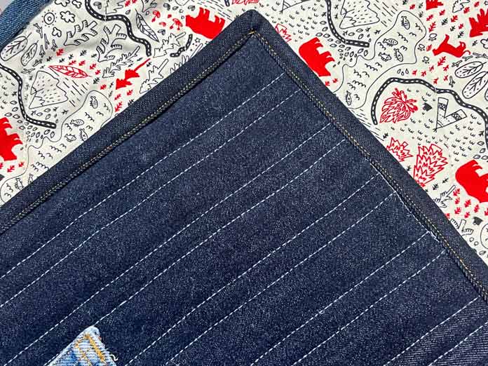 The binding is sewn down on a denim quilt using a gold-colored thread.