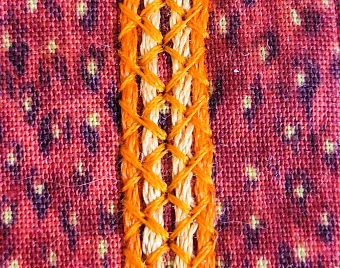 An orange thread holding orange embroidery floss to an orange fabric