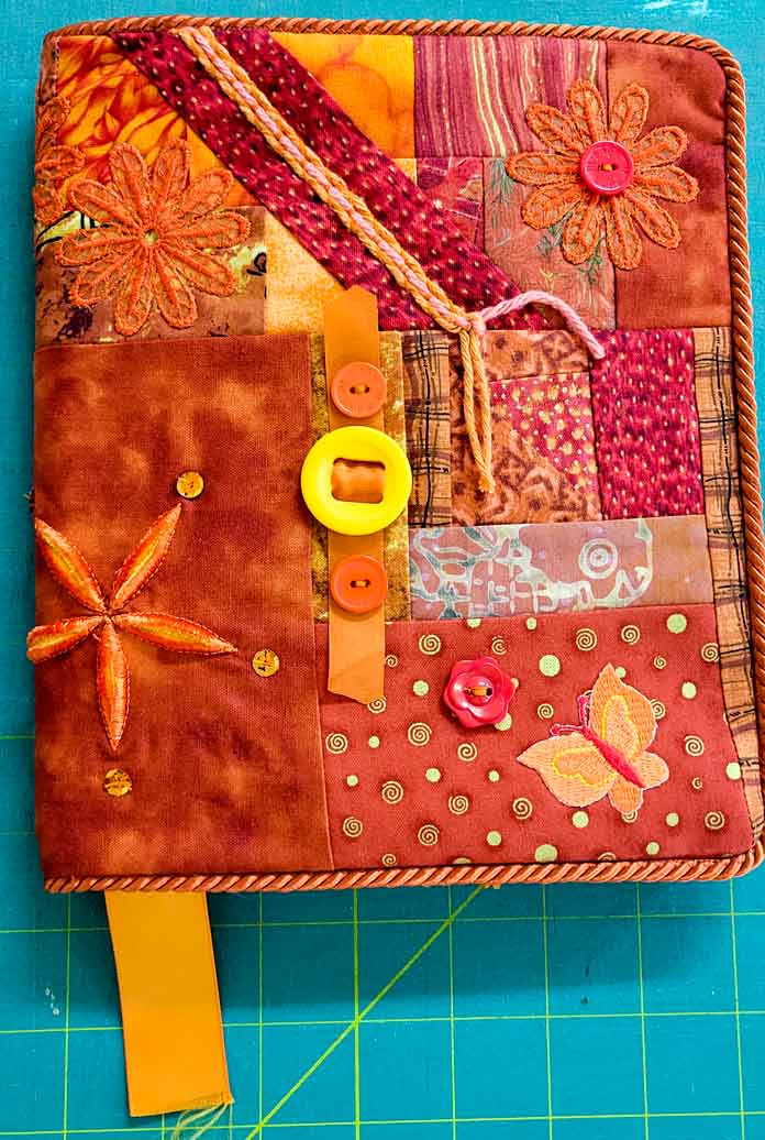An orange journal cover embellished with buttons, ribbons, and machine embroidery