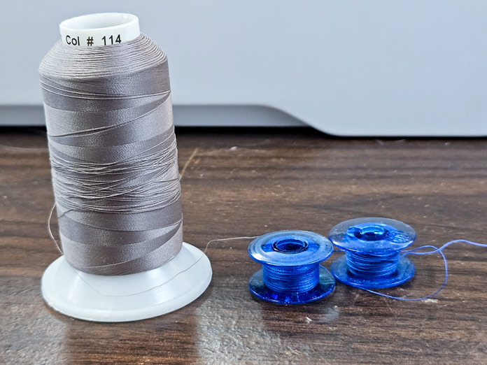 A spool of beige thread with two blue bobbins with blue thread