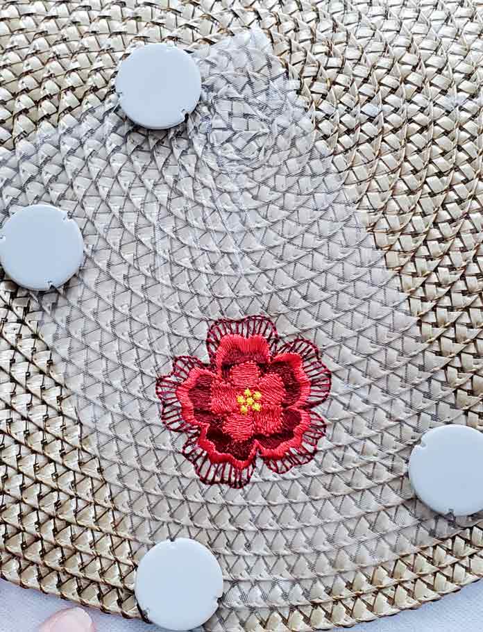 A floral motif in shades of red on a synthetic rattan table topper using a metal embroidery hoop; Small Metal Hoop (100 by 100mm), INSPIRA Magnets for Metal Hoop