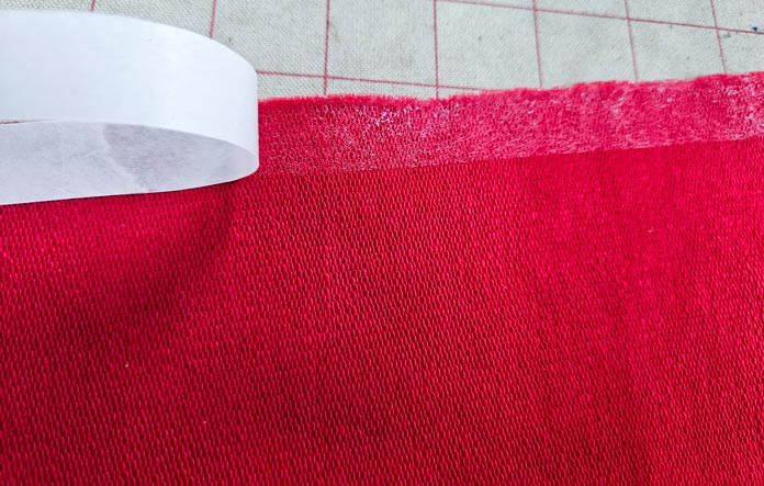 A white strip pulling away from a red fabric; Learn how to use HeatnBond SOFTSTRETCH fusible web on knits, denim, fleece, and more