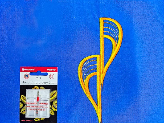 One package of machine embroidery twin needles on blue fabric with a yellow embroidery on the right; machine embroidery, quilting, applique, cutwork embroidery, free-standing lace, embroidery techniques, HUSQVARNA VIKING, Designer Epic 3, mySewnet, JoyOS Advisor