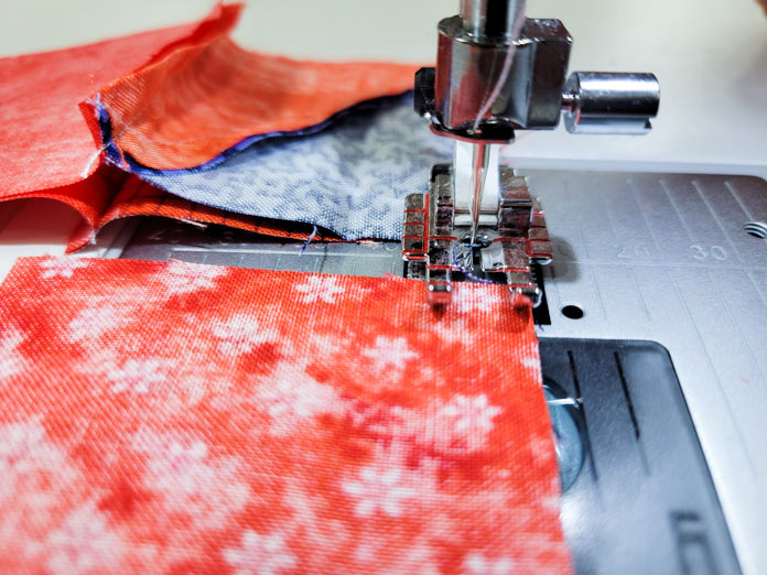 An orange piece of fabric under the presser foot on a sewing machine; Husqvarna Viking Tribute 150C