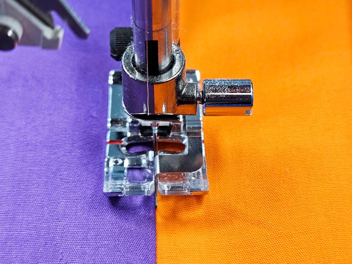 A metal presser foot on purple and orange fabrics; Husqvarna VIKING DESIGNER EPIC 3