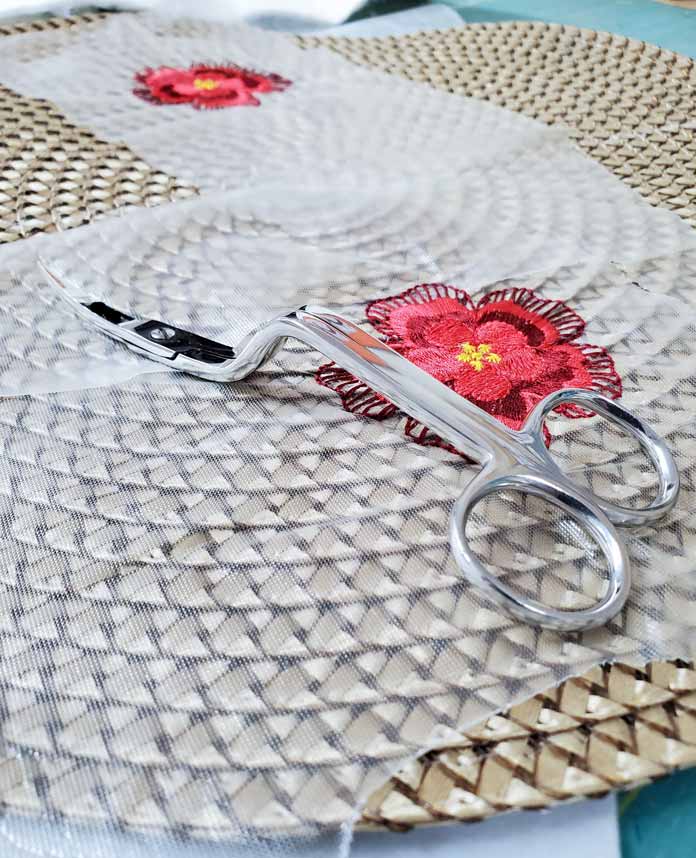 A pair of curved handled embroidery scissors on top of the embroidered synthetic rattan table topper; INSPIRA 6" Double Curved Embroidery Scissor