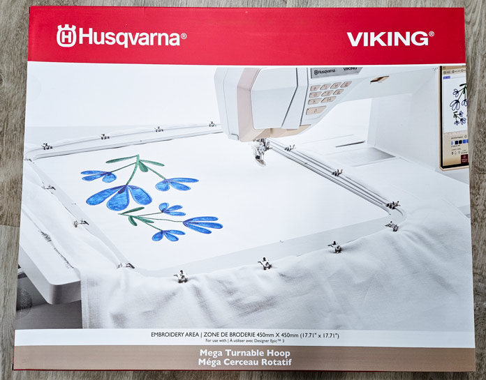 A red and white box with an embroidery hoop Husqvarna VIKING DESIGNER EPIC 3 sewing and embroidery machine; Husqvarna VIKING 6in/15.2cm Applique Scissor, Husqvarna VIKING Open Toe Presser Foot for IDF System, Husqvarna VIKING Mega Turnable Hoop 450 mm x 450 mm, Husqvarna VIKING Tear-a-Way Extra Wide Stabilizer 24" x 10 Yards, Husqvarna VIKING Cut-a-Way Extra Wide Stabilizer 24” x 10 Yards, SULKY Slimline Metallic Dream Assortment