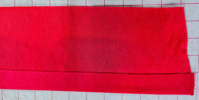 A piece of red fabric on an ironing surface; Learn how to use HeatnBond SOFTSTRETCH fusible web on knits, denim, fleece, and more