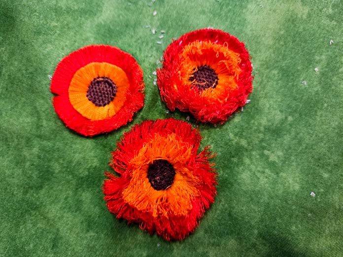 Three orange and gold flowers stitched on green