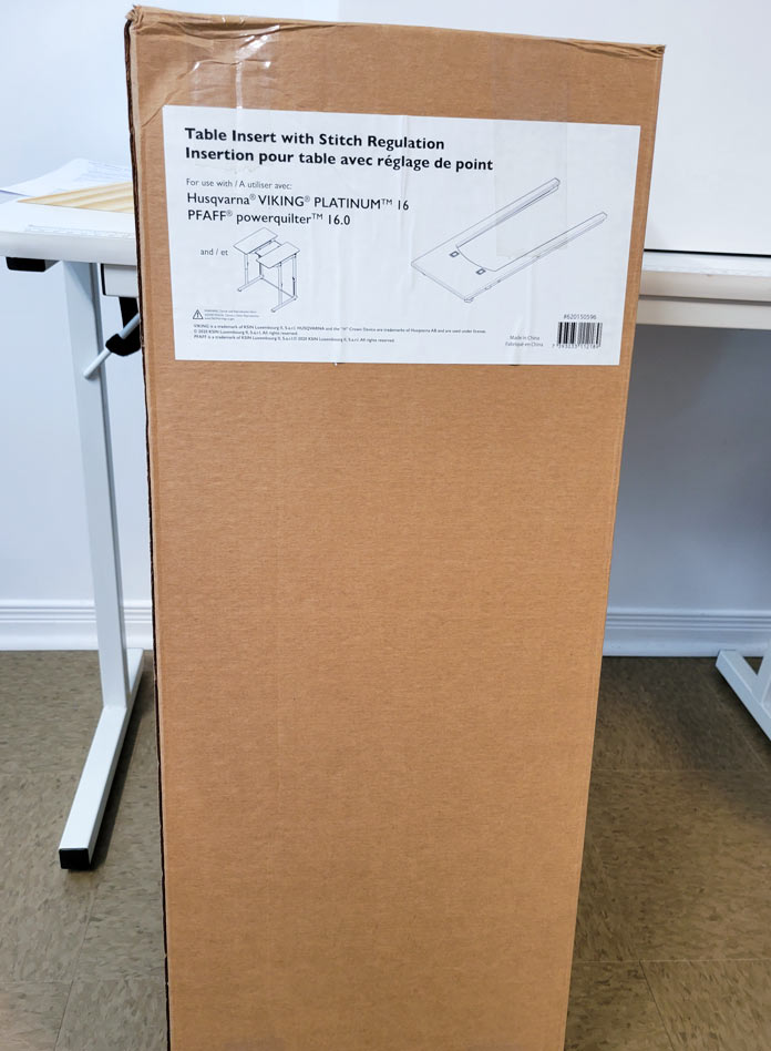 A cardboard box containing a stitch regulator in front of the white sewing machine table