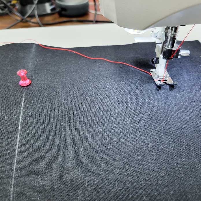 A pink push pin with a sewing machine foot on black fabric; Gütermann topstitching threads, Husqvarna Viking Tribute 150C