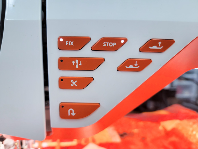 Seven orange buttons on a white sewing machine; Husqvarna Viking DESIGNER EPIC 2