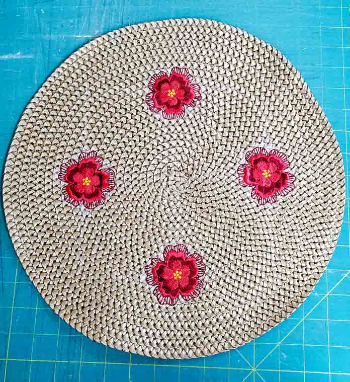 Four red, machine embroidered floral motifs on a round synthetic rattan table topper