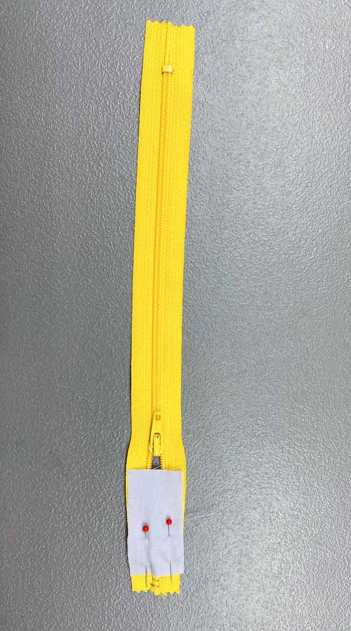 A small piece of gray fabric pinned to a yellow zipper; COSTUMAKERS General Purpose Closed End Zipper