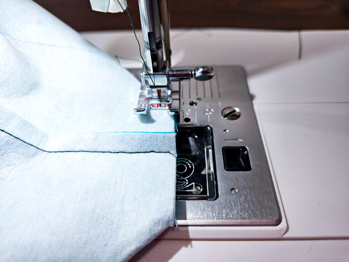 White fabric under a metal presser foot on a sewing machine