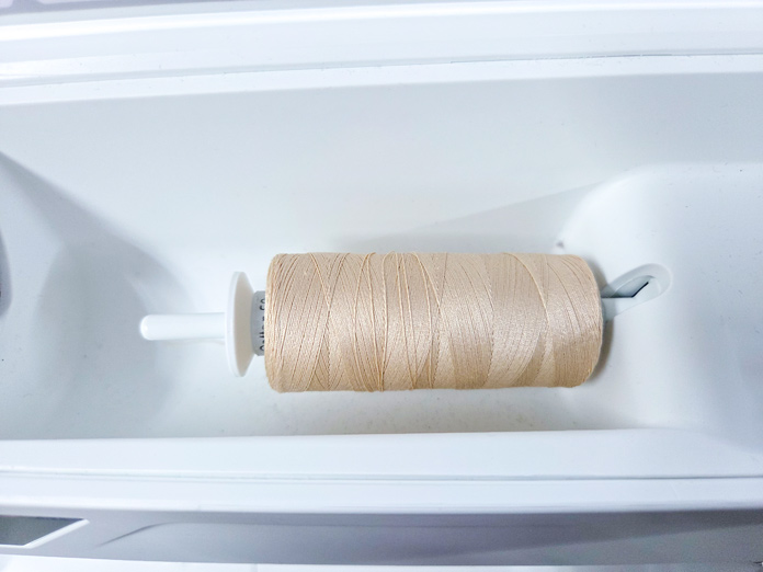 A spool of thread in a horizontal position on a sewing machine