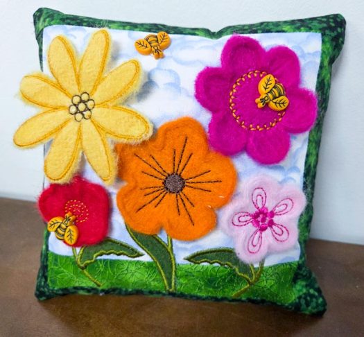 Five felted flowers on a blue and green cushion