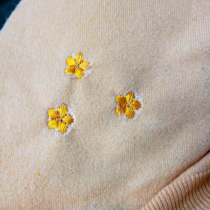 Three orange embroidery flowers on an orange sweater; Inspira Water Works Soluble Film