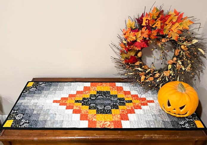 Table runner on a wooden chest with a fall wreath and a pumpkin off to the side