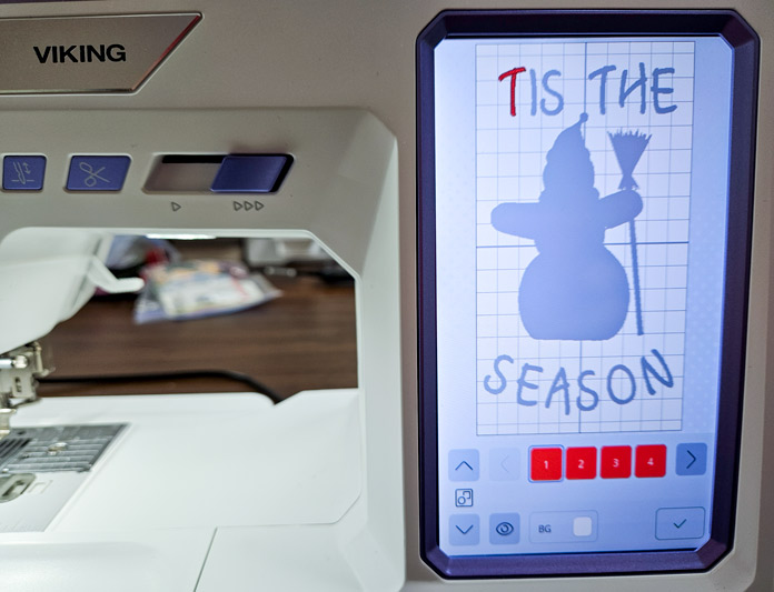 A screen on a computerized embroidery machine shows the shape of a snowman and some writing with the letter t highlighted in red; Husqvarna VIKING Designer Quartz 29, mySewnet Machine Embroidery Software, Husqvarna VIKING Tear-a-Way Light Stabilizer 15 Inches x 25 Yards