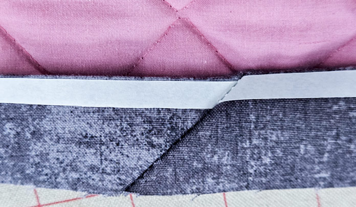 A strip of grey fabric, a white strip of paper, and a strip of pink fabric; HeatnBond Lite, quilt binding, fusible web, fabric crafts