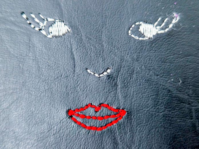 A face stitched on black vinyl in red and white thread