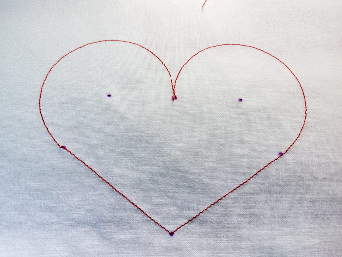 A heart stitched in red thread on white fabric