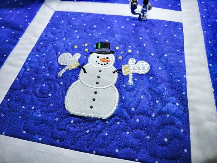 A white snowman on blue fabric with blue stitching; PFAFF powerquilter 1600