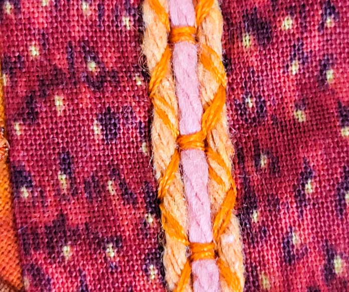 Three stands of orange yarn on an orange fabric