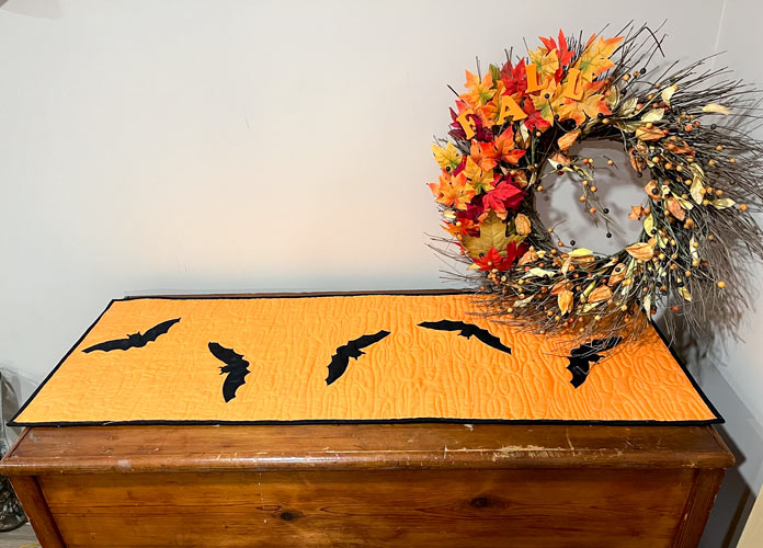 Reverse side of the table runner with bats on it on a wooden chest with a fall wreath off to the side